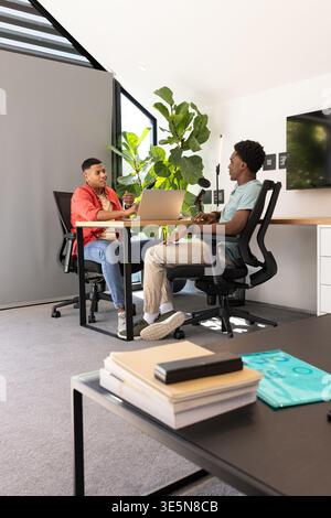 Talking Diverse male coworkers sharing ideas at desk in meeting room, with laptop and microphone Stock Photo