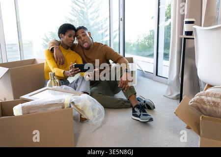 Smiling couple taking selfie on carpeted floor in new apartment, with boxes and bubble wrap Stock Photo