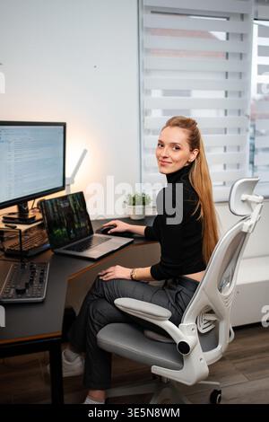 Smiling woman working at desk with laptop and monitor Stock Photo