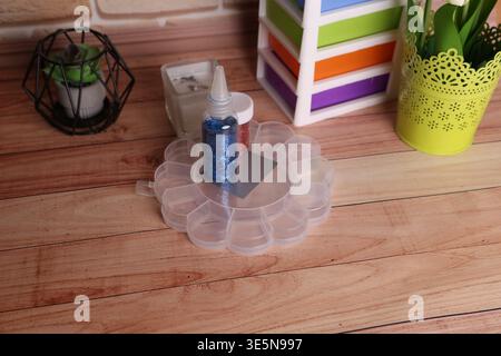 A crafting area shows a clear storage container holding glitter next to colorful supplies. A small plant is nearby, adding to the workspace scene Stock Photo