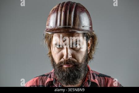 Bearded man worker with beard in building helmet or hard hat. Portrait of confident worker in helmet isolated on grey background. Man builders Stock Photo