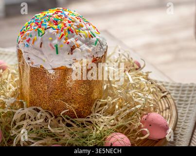 Easter cake with white icing and colorful sprinkles in basket with eggs festive spring composition Stock Photo