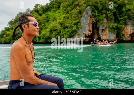 Thai fisherman relaxing on boat viewing limestone islands Stock Photo