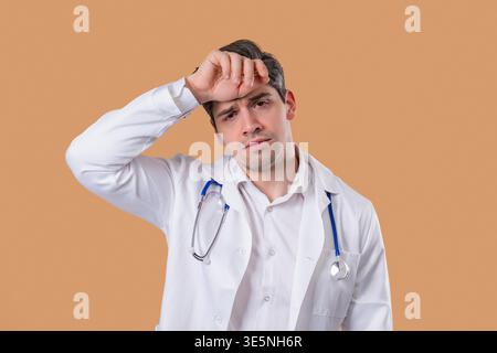 30s aged physician man in white medical coat form having headache, studio portrait. Guy putting hands on head, isolated on warm yellow background. Concept of problems, medicine, illness Stock Photo