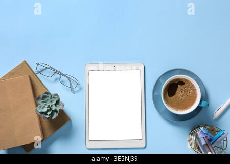 Tablet computer with cup of coffee, eyeglasses and stationery on blue background Stock Photo