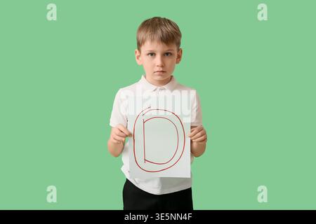 Sad schoolboy holding paper with grade on green background Stock Photo