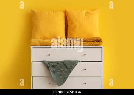 Pillows with folded blankets on commode near yellow wall Stock Photo