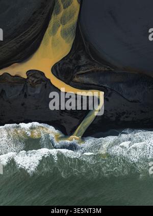 Aerial view of a vibrant river snaking through dark sands, meeting the frothy, churning ocean in a stunning display of natural contrast, south of Icel Stock Photo