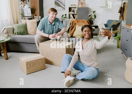 Black Woman Taking Selfie While Packing Donation Boxes at Home Stock Photo