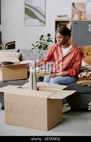 Black Woman Sorting Clothing Donations for Charity Drive at Home Stock Photo