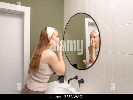 Young woman applying moisturiser during a skincare routine. Morning beauty and wellness moment focused on healthy skin, hygiene, and self-care at home Stock Photo