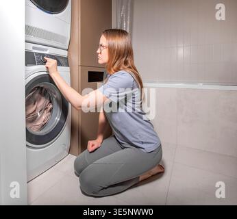 Woman selects laundry program on washing machine control panel. Closeup of hand turning dial on modern household appliance during domestic routine. Stock Photo