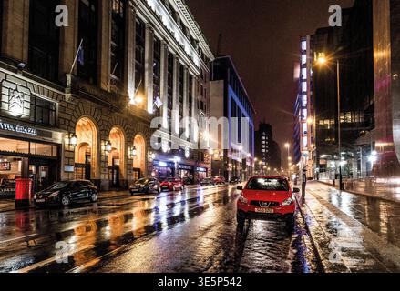Empty urban street at night on Bothwell Street, wet pavement reflecting warm building lights and a parked red car. Moody, cinematic cityscape with gli Stock Photo