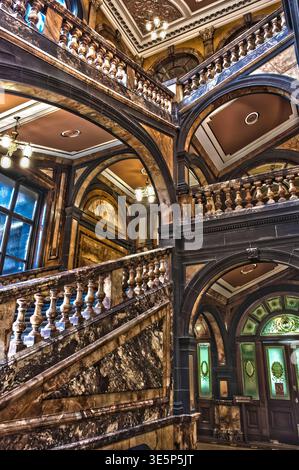 Ornate marble stairway and carved balustrades fill a historic city chambers interior with grand arches, warm lighting and detailed ceiling decoration, Stock Photo
