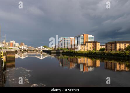 Finnieston riverside scene showing a white pedestrian bridge and modern office buildings reflected in the calm river, dramatic storm clouds overhead a Stock Photo