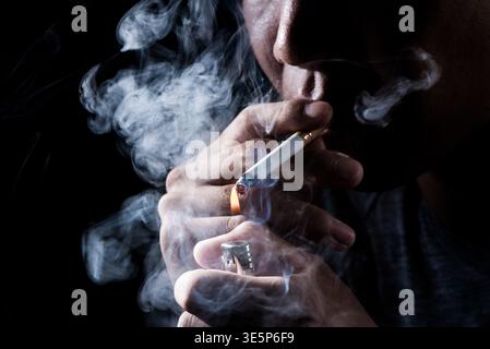 Man holding a cigarette and lighter, beginning to light the tobacco Stock Photo