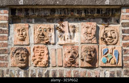 Artistic installation with mask and facial reliefs made of terracotta, in a historic brick wall, Warburg, North Rhine-Westphalia, Germany, Europe Stock Photo