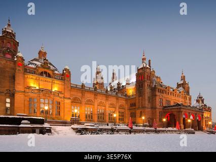 Historic Kelvingrove Art Gallery and Museum in Glasgow illuminated at dusk, surrounded by snow and festive Christmas lights. Warm sandstone glow contr Stock Photo