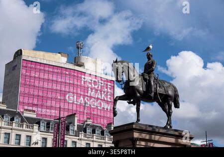 An equestrian statue in George Square, Glasgow, framed against a bright pink 'People Make Glasgow' building with a seagull perched on the rider, evoki Stock Photo