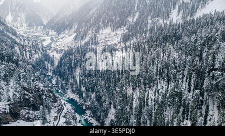 Aerial view of the dazzling contrast of the turquoise river cutting through the snow-laden forest, Sharda, Azad Kashmir, Pakistan. Stock Photo