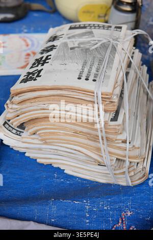 Stacked newspapers with Japanese characters on their pages, tied securely with white string, resting on textured blue tarp surface, ready for Stock Photo