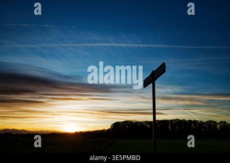 A sign points the directions of a path and is silhouetted against a winter sunset with a woodland in the distance, Sprotbrough, Doncaster. Stock Photo