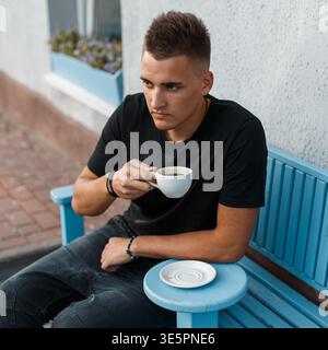 Handsome young man sitting outdoors in a cafe and drinking coffee Stock Photo