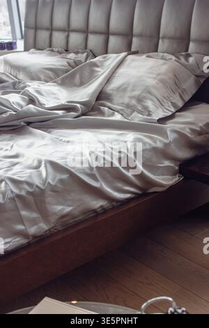 Grey silk sheet on a bed. Luxury bed linen. Hotel bedroom concept. Comfortable bed with fabric and two pillows. Double bed for couple. Messy bedding Stock Photo