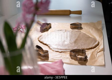 Springtime baking happens in the kitchen with rolled gingerbread dough prepared for Easter cookies. Cookie cutters shaped like bunnies and eggs are ready for use. Flowers add color to the scene. Stock Photo