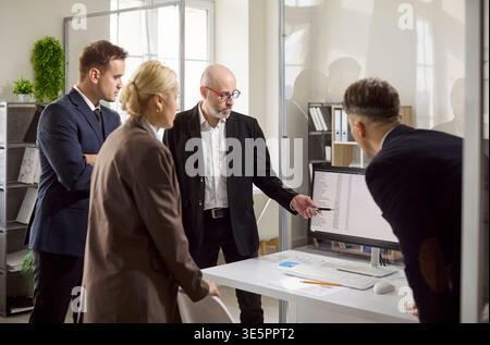 Manager pointing at data on monitor during office meeting with analytical team Stock Photo