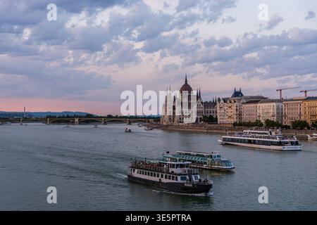 BUDAPEST, HUNGARY - SEP 7, 2025: Sightseeing cruise boats on the Danube river at twilight with the Hungarian Parliament and Margaret Bridge behind. Stock Photo