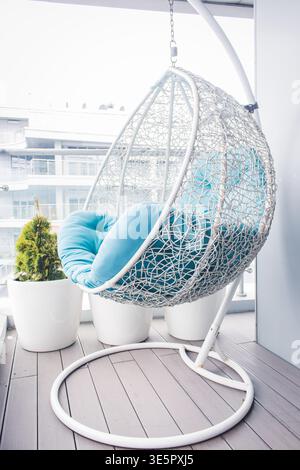Cozy modern apartment concept. Cozy wicker hammock on balcony. Hanging chair with a blue pillow on wooden terrace. Luxury house design. Dream house Stock Photo