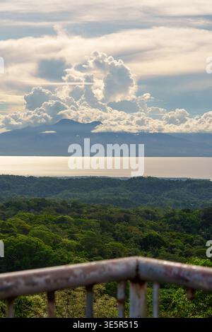 Mount Bandilaan, Siquijor, Philippines – April 12, 2025: A lookout view shows forest canopy, the sea, and a distant island beneath towering clouds. Stock Photo