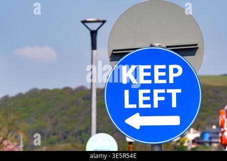 Round Keep Left sign with white letters on a blue background isolated against a defocused background. No people. Stock Photo