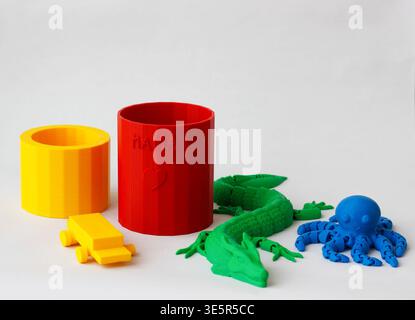 Colorful 3d printed objects including cups, toy car, dragon and octopus on white background, modern additive manufacturing concept, creative hobby Stock Photo