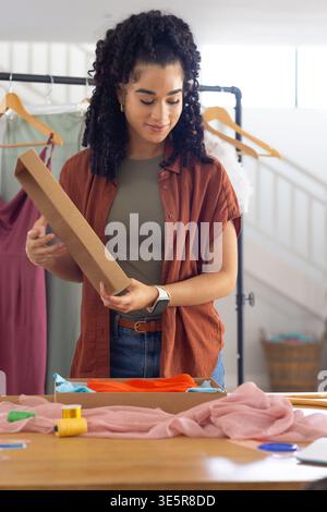 Adult female handling rectangular box lid while packing folded garments wrapped in tissue at studio Stock Photo