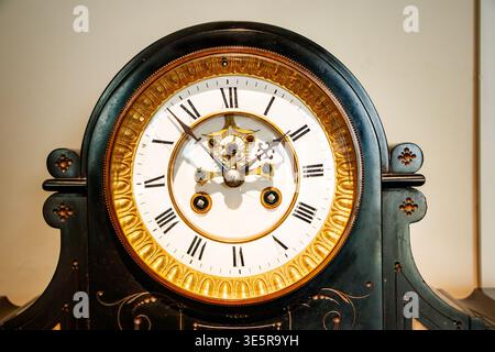 Vintage mantel clock featuring a white dial face with Roman numerals & ornate brass details Stock Photo