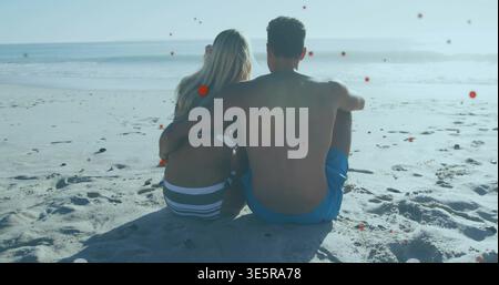 Watching gentle waves rolling, couple sitting close and embracing on beach, wearing swimsuits Stock Photo