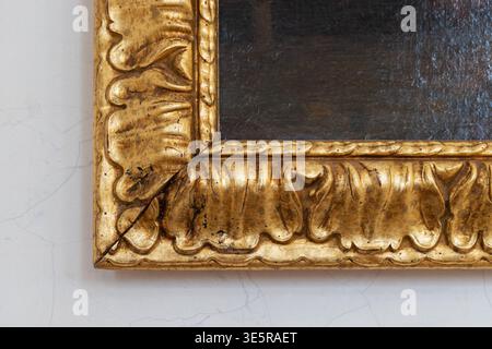 Gilded wooden picture frame corner with intricate decorative elements and artistic carving details against a white wall background, symbolizing luxury Stock Photo