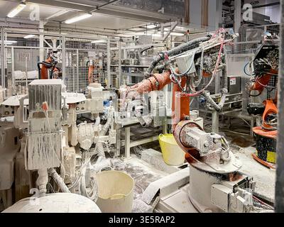 Industrial robotic arm covered in white ceramic slip at a sanitary ware manufacturing plant Stock Photo