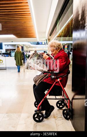 London UK, April 02 2026, An Old Lady Sitting in her Walker or Rollator Reading a Daily Newspaper Alone Stock Photo