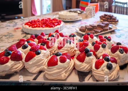 party Table with various desserts including pavlova topped with strawberries and blueberries chocolate brownies and a fruit tart Stock Photo