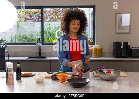 African American woman in denim preparing food on marble kitchen island cutting avocados with knife Stock Photo