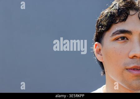 Asian man looking slightly off camera against blue gray wall wearing white T-shirt, copy space Stock Photo