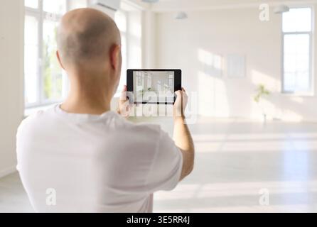 Male designer holding tablet assessing interior space in minimalist bright hall Stock Photo