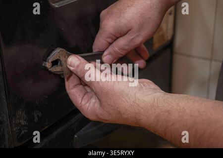 Close-up of a hands using an adjustable wrench to tighten a bolt on the exterior of an oven door in a home kitchen. Stock Photo