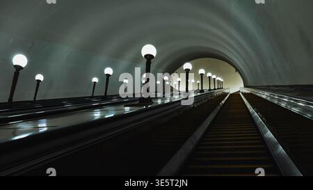 Escalators ascending through a long, illuminated underground tunnel in Moscow Metro Stock Photo