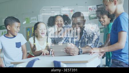 Gathering adult male teacher and five students leaning around desk, viewing tablet with HUD overlay Stock Photo
