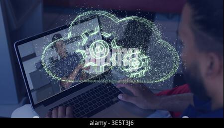Watching man wearing dark shirt using laptop at home, showing holographic cloud with gears Stock Photo