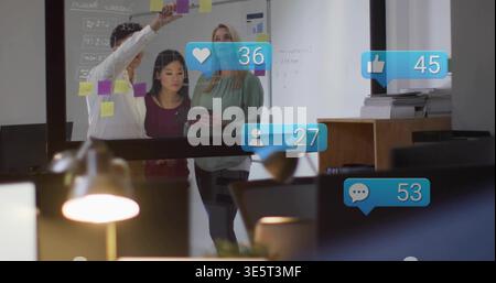 Collaborating three colleagues in smart casual placing sticky notes on glass in office with tablet Stock Photo